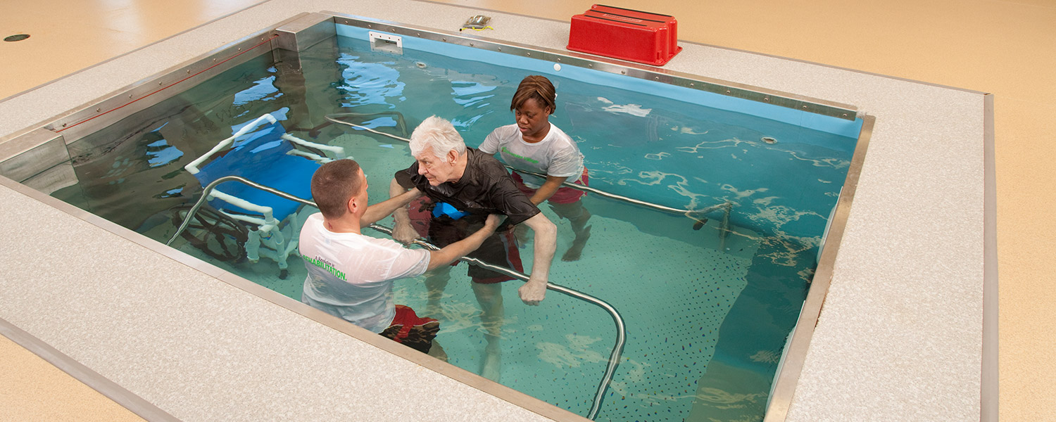 Trainers helping a person train in pool