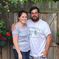 Two people posing for a photo in front of a fence