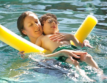 Person holding child on floating device in pool