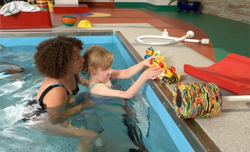 Adult holding child in pool with rubber ducks