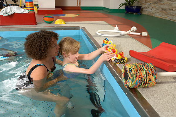 Adult holding child in pool with rubber ducks