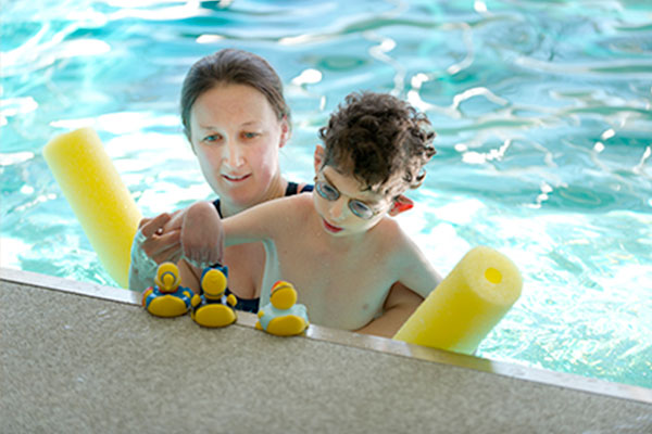 Person holding child in pool with rubber ducks