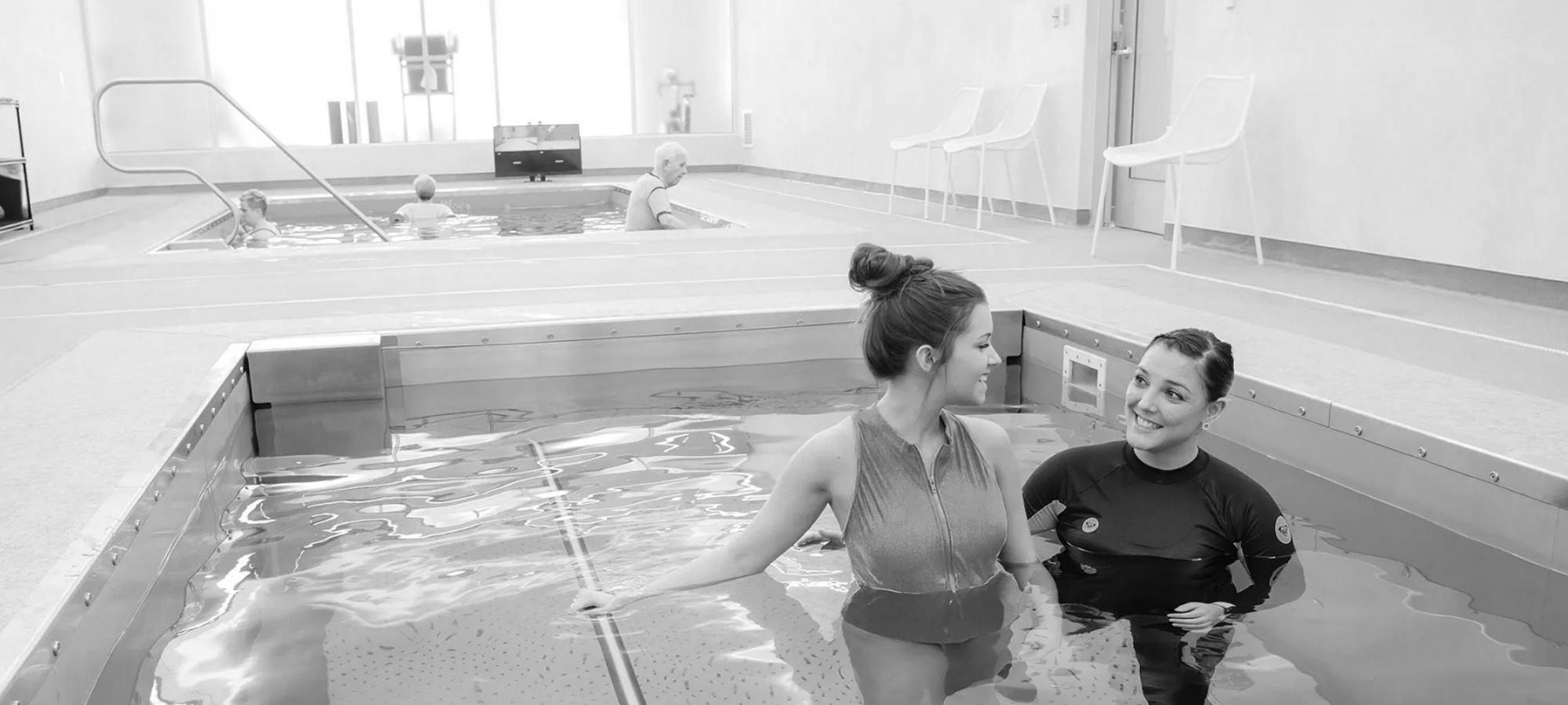 trainer working with female athlete in pool black and white